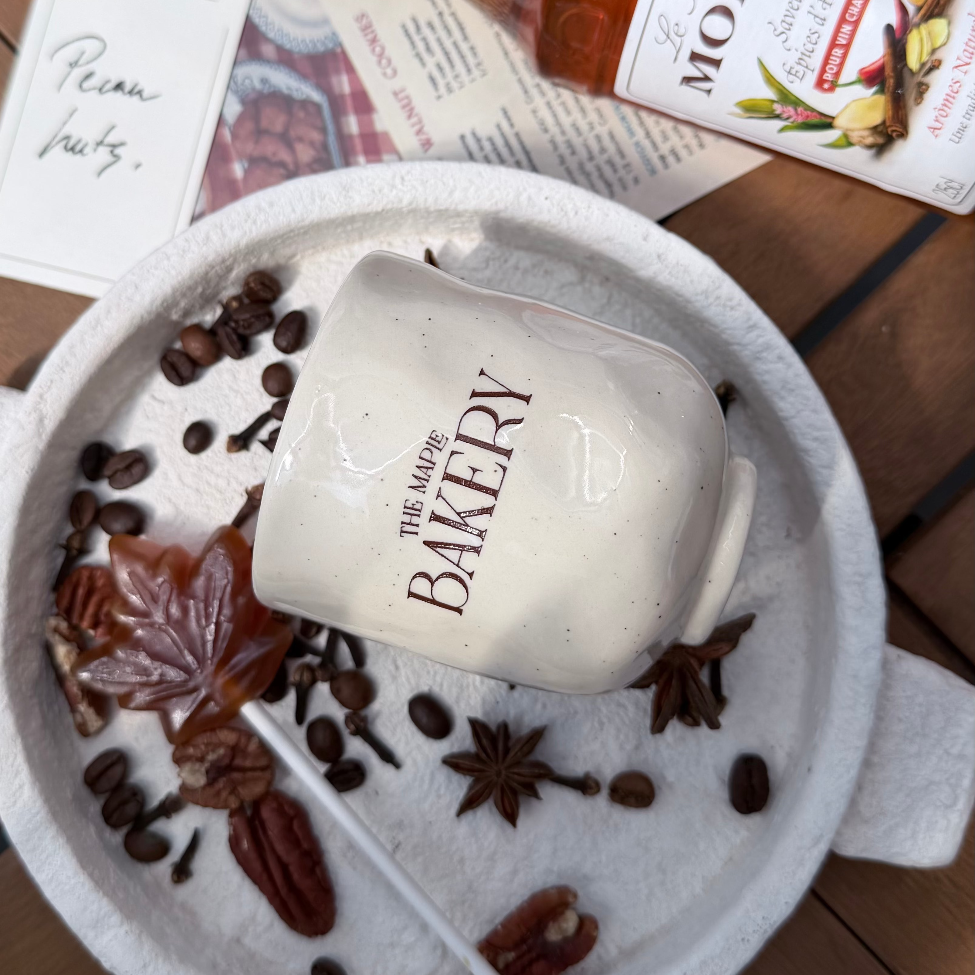 Mug The Maple Bakery posé dans un plateau d'épices d'automne : cannelle, anis étoilé, café et feuille d'érable